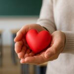 Hands holding a red heart shape in a classroom setting without visible text or logos